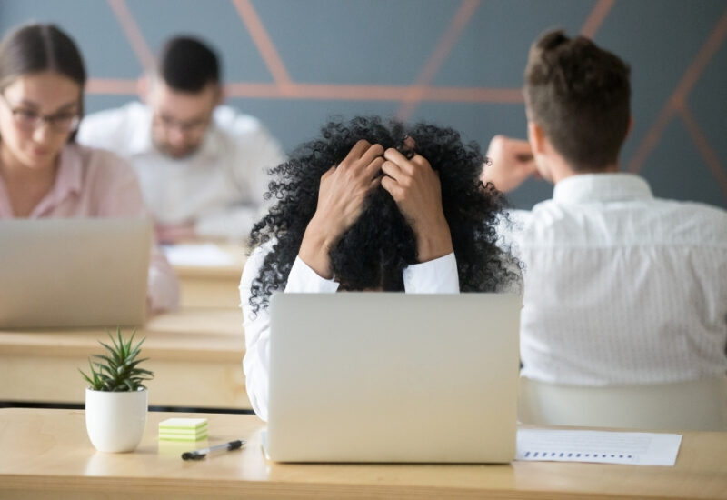 user-inserted A woman sits at a desk, resting her head in her hands, conveying a sense of stress or overwhelm.